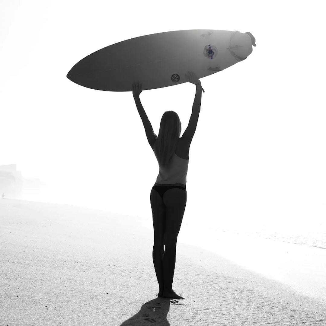 Person holding a surfboard above their head on a beach