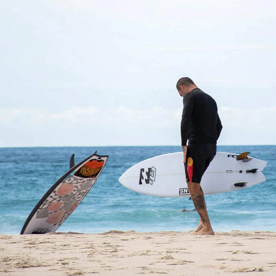 a man standing on a beach next to a surfboard